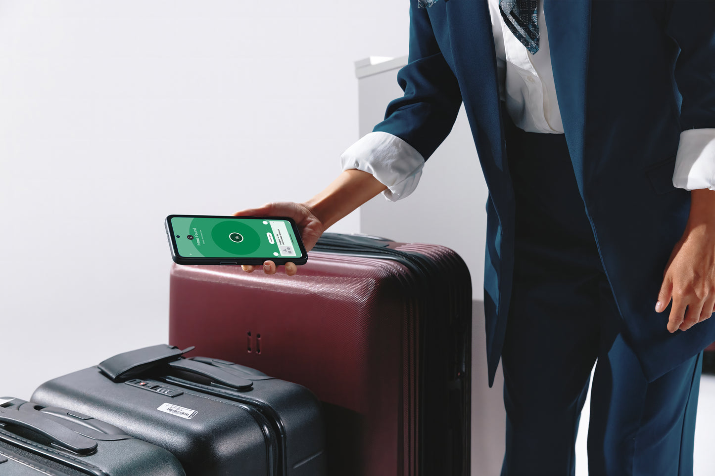 Person in a suit using a smartphone app on a suitcase with another suitcase nearby.